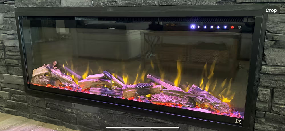 Touchstone Sideline Elite Pro Electric fireplace with glowing logs and flames against a stone wall.