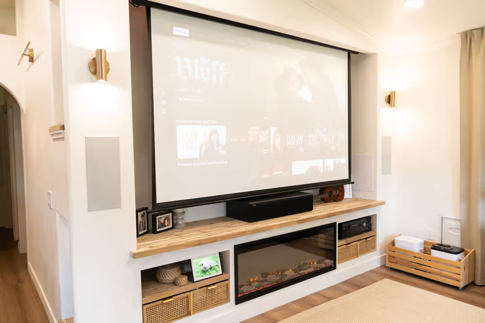 Modern living room with a large screen TV, fireplace, and decorative items.