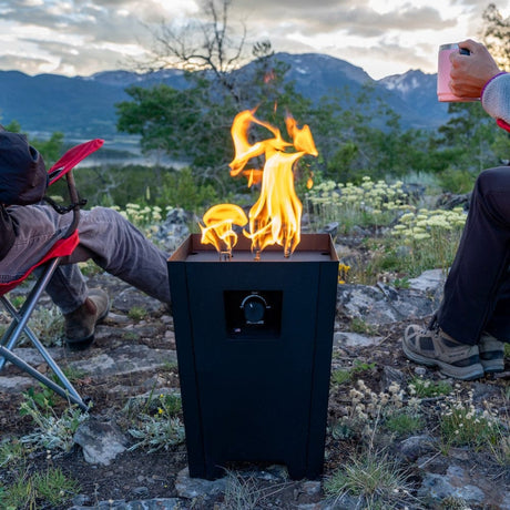 The Live Outdoor Firestorm Series I Portable Propane Fire Pit is being used outdoors with people sitting nearby.