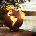 Fire Pit Art Third Rock - Globe Shaped 36" Handcrafted Carbon Steel Fire Pit (TR) Lit Up Beside A Lake