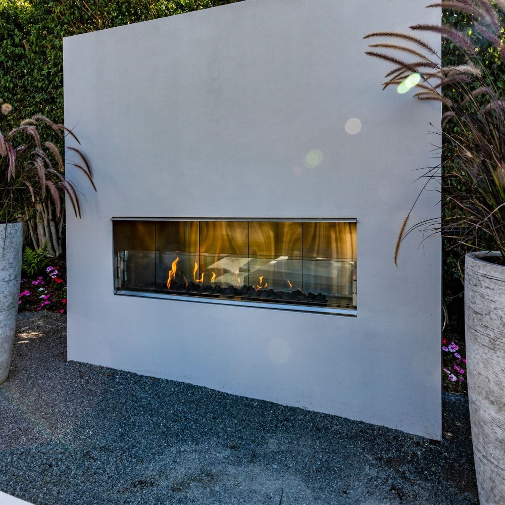 firegear kalea bay outdoor gas fireplace with white surround in backyard