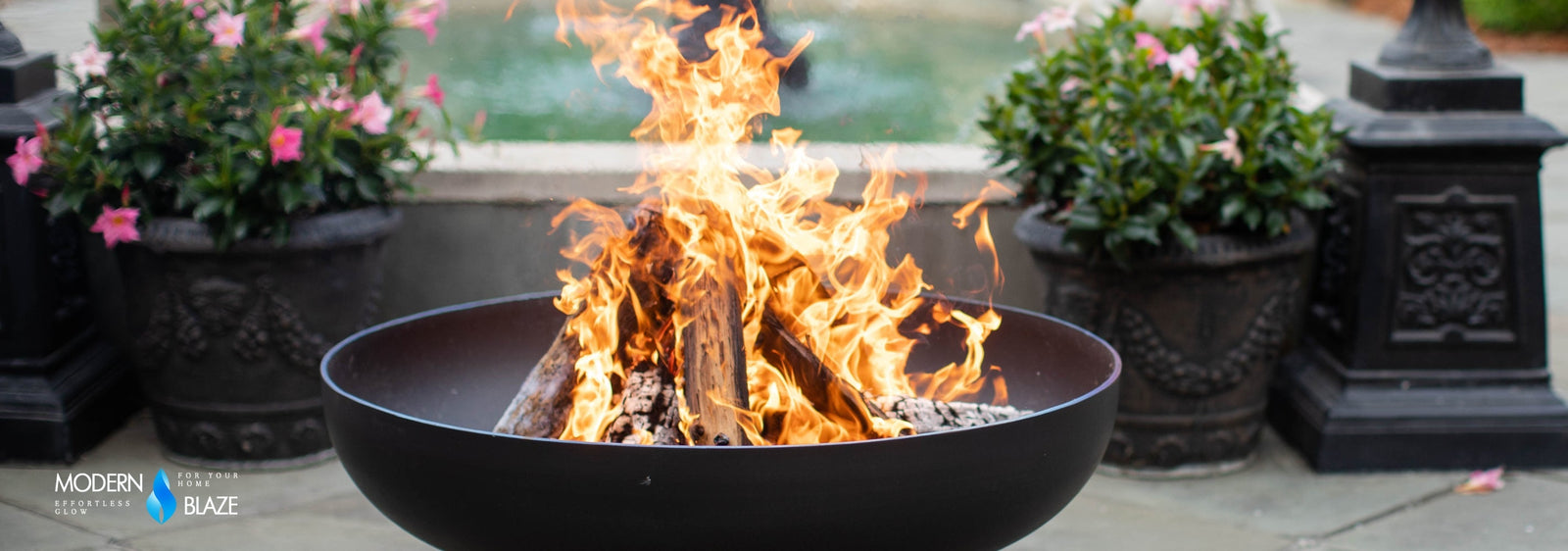 Seasons Fire Pit with burning wood, surrounded by potted plants and a fountain