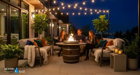 People around a lit dining-height wooden barrel gas fire pit table on an outdoor terrace at dusk