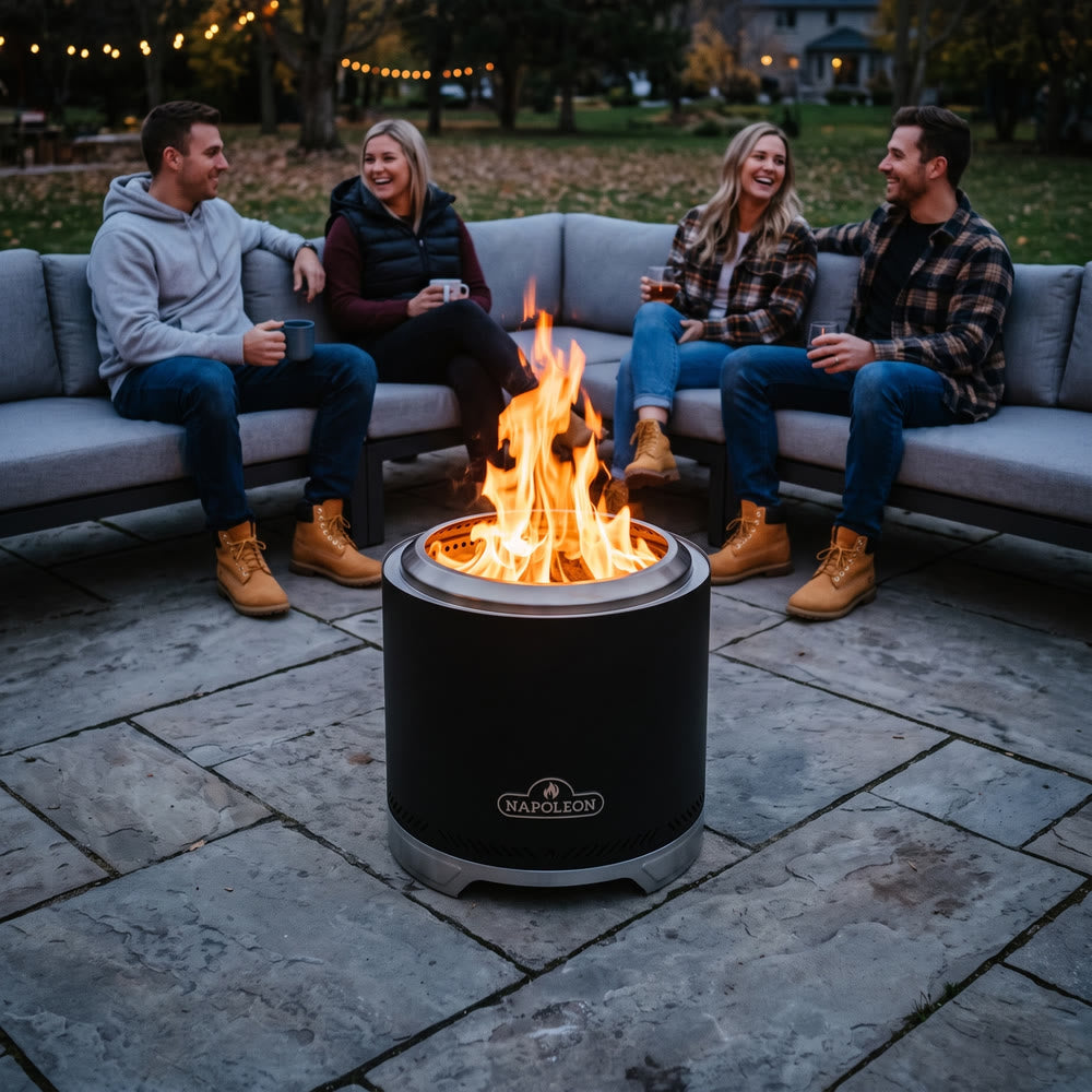 Napoleon Timberwolf 18-Inch Fire Pit in Matte Black on a stone patio with friends on an outdoor sectional at dusk