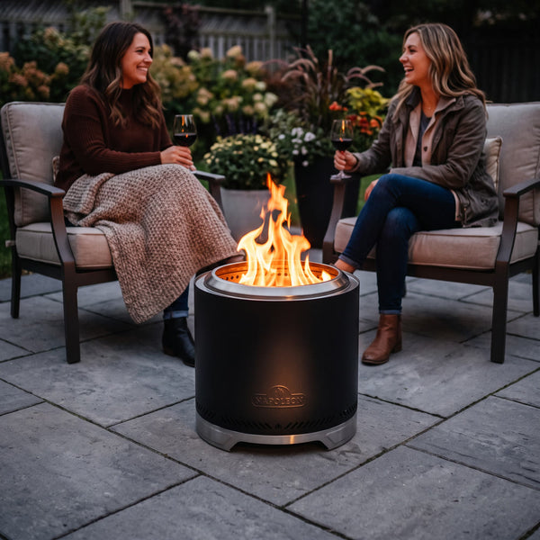 Napoleon Timberwolf 18-Inch Fire Pit in Matte Black on a small stone patio with two friends holding wine