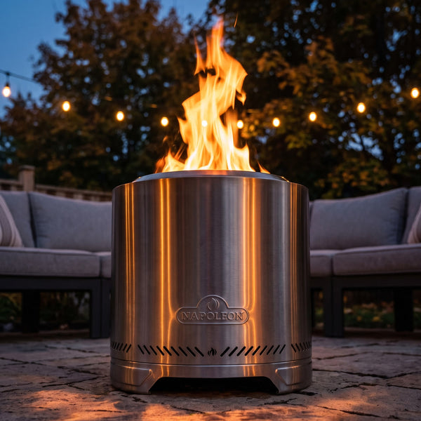 Napoleon Timberwolf 18-Inch Fire Pit in Stainless Steel lit on a stone patio at twilight