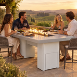 Couples dining on a vineyard terrace at golden hour around a Top Fires Alameda 72-inch GFRC gas fire table with a Metallic Pearl tabletop and White base
